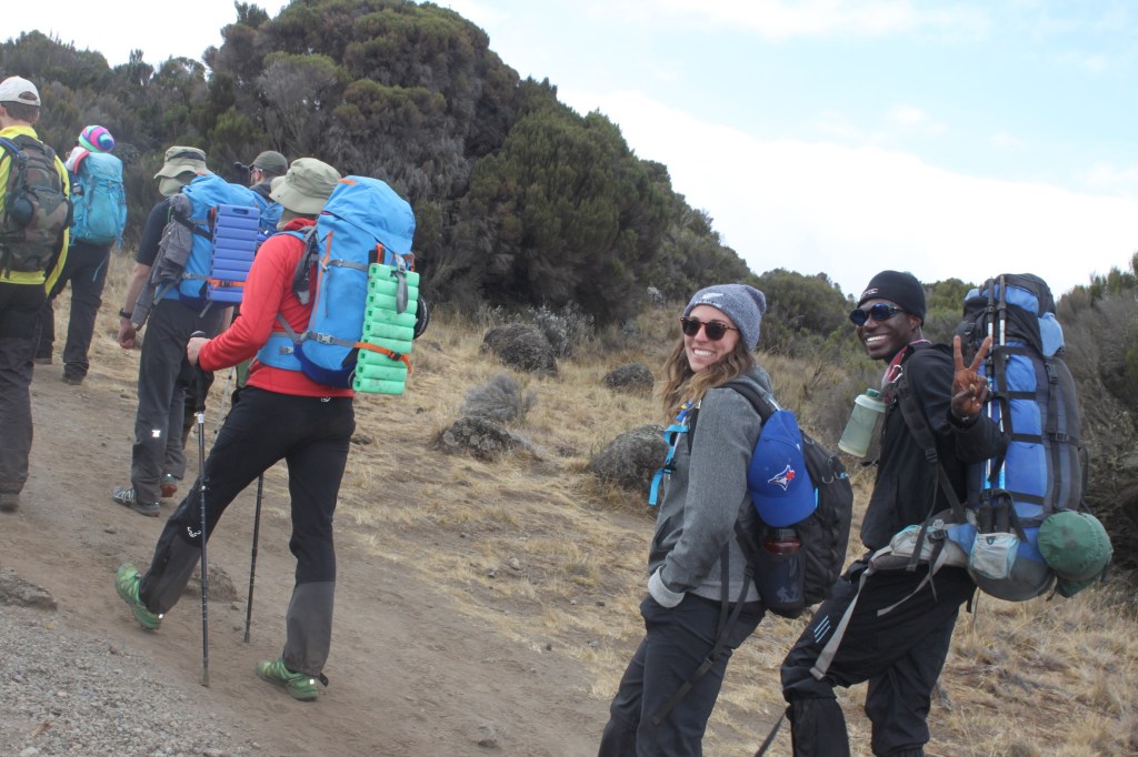 Two smiling trekkers walking up to the top of Mount Kilimanjaro.