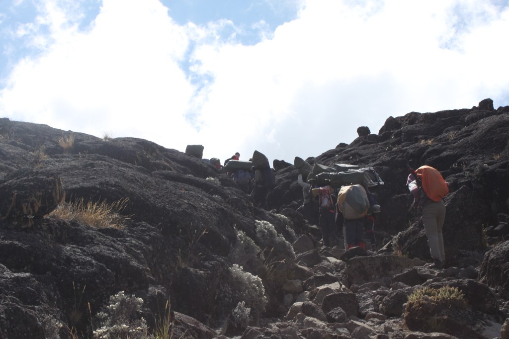 Looking upwards at porters carrying heavy bags up the Barranco Wall on a trek up Mount Kilimanjaro. 