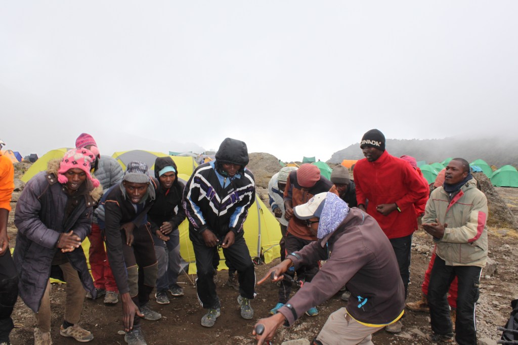 A group of porters dance and sing in a circle on a trek to Mount Kilimanjaro. 